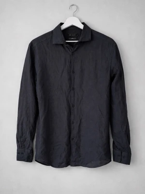 Svart linneskjorta från Riley - Stilren svart skjorta från Riley i 100% linne. Skjortan har lång ärm, klassisk krage och knäppning framtill. Slim fit-modell som ger en snygg och modern siluett. Perfekt för dig som gillar en enkel men trendig look.