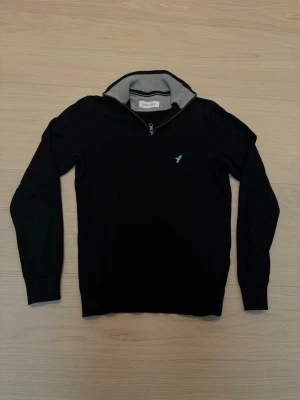 Svart stickad tröja med halv dragkedja Pier One - Stilig svart stickad tröja från Pier One med halv dragkedja och grå insida på kragen. Tröjan har långa ärmar och en riktigt fin logga på bröstet. Perfekt för lager på lager och enkel att matcha.