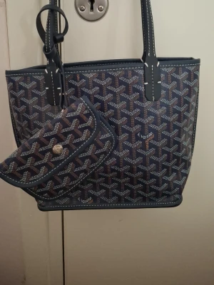 Blå  handväska med mönster - Snygg blå handväska med klassiskt grafiskt mönster i vitt och brunt. Väskan har två axelband och kommer med en matchande liten clutch. Perfekt för dig som gillar exklusiva accessoarer.