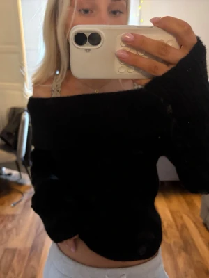 Svart off shoulder stickad tröja - Snygg svart stickad tröja med off shoulder-modell och långa ärmar. Tröjan har en bred krage som vilar över axlarna och är perfekt för en trendig och avslappnad look. Mjuk och skön att bära, passar till många olika outfits.