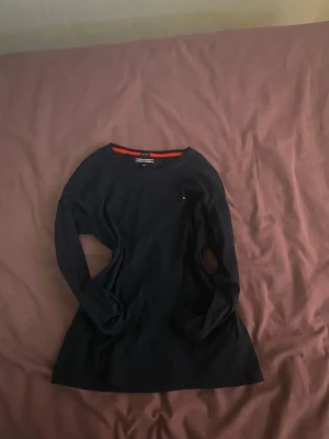 Mörkblå långärmad topp Tommy Hilfiger - Snygg mörkblå långärmad topp från Tommy Hilfiger i ekologisk bomull. Rund halsringning med röd detalj på insidan av kragen och diskret logga på bröstet. Perfekt basplagg för en clean och stilren look.