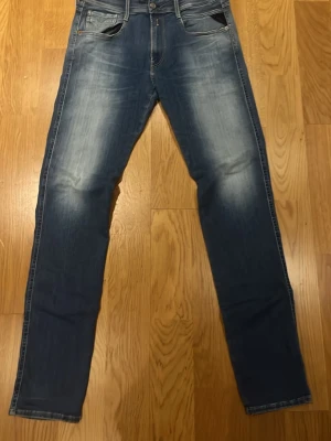 Blåa replay anbass jeans med slitningar W32 L34 - Säljer ett par blå replay jeans med snygga slitningar och tvättade detaljer på låren och knäna. Klassisk femficksmodell med raka ben och normal midja. Perfekta för en avslappnad och trendig look.