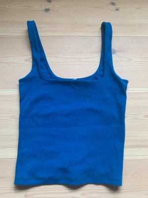 Blå ribbad linnetopp från Zara - Säljer en blå ribbad linnetopp från Zara med breda axelband och rundad urringning. Perfekt att styla med jeans eller kjol för en enkel och snygg look. Materialet är mjukt och stretchigt för extra komfort.