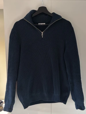 Mörkblå stickad tröja med dragkedja - Mörkblå stickad tröja från Zara med halv dragkedja och krage. Tröjan har ribbstickad struktur, långa ärmar och en avslappnad passform. Perfekt för lager-på-lager och enkel att matcha med jeans.
