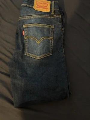 Mörkblå Levi's jeans med klassisk passform - Snygga mörkblå jeans från Levi's med klassisk femficksdesign och kontrastsömmar. Jeansen har en rak passform och är tillverkade i slitstarkt denim med den ikoniska läderpatchen bak i midjan.