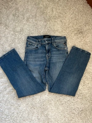 Blå raka jeans från Replay - Snygga blå jeans från Replay med rak passform och klassisk femficksdesign. Jeansen har en mellanblå tvätt med lätt slitning och Replay-logga på bakfickan. Tillverkade i mjuk denim som ger en skön känsla och stilren look.