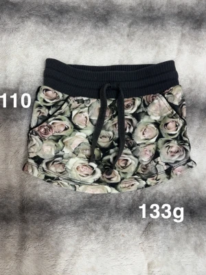 Blommig kjol med snörning - Supersöt kjol med blommigt mönster i rosa och gröna toner. Kjolen har bred svart resår i midjan och snörning framtill för extra passform. Perfekt för dig som gillar en bekväm och trendig stil.🌸Fint använt skick. Storlek 110 