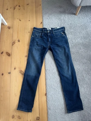 Mörkblå jeans från Replay - Helt nya snygga mörkblå jeans från Replay med klassisk femficksdesign och raka ben. Jeansen har diskreta slitningar och tydliga sömmar, samt logotypdetalj vid fickan. Perfekta för en stilren och avslappnad look. Original pris är 1200kr och alla prislappar är kvar