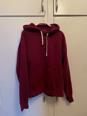 Vinröd hoodie från Polo Ralph Lauren - Snygg vinröd hoodie från Polo Ralph Lauren med klassisk huva och vita dragsnören. Skriv vid funderingar!