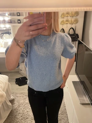 Ljusblå stickad tröja med puffärm - Supersöt ljusblå stickad tröja med korta puffärmar och rund halsringning. Tröjan har ribbstickade muddar vid ärmslut och nederkant. Perfekt för dig som gillar en trendig och mysig look.