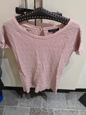 Ljusrosa topp från Ilse Jacobsen - Supersöt ljusrosa topp från Ilse Jacobsen med korta ärmar och rund halsringning. Toppen har ett diskret strukturmönster i tyget och en liten knappdetalj bak i nacken. Perfekt att styla med jeans eller kjol.