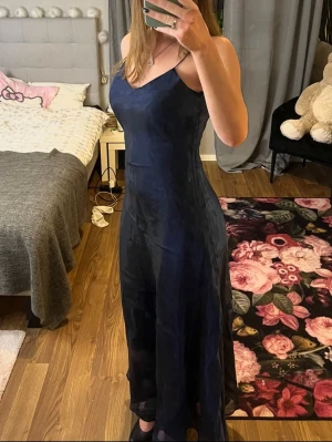 Mörkblå långklänning med tunna band - Elegant mörkblå långklänning med tunna elastiska axelband och v-ringad halsringning från Rosay. Klänningen har en slät, glansig yta och ett figurnära fall som ger en stilren siluett. Storlek 36. Skriv om funderingar och priset kan diskuteras 💙