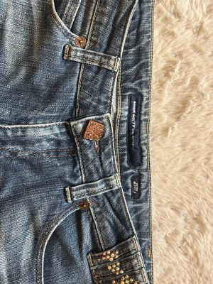 Blå Miss Sixty jeans med raka ben - Snygga blå jeans från Miss Sixty med raka ben och klassisk femficksdesign. Jeansen har slitningar och ljusare partier för en cool, använd look. Detaljer i kopparfärg och små nitar vid fickan ger extra stil. Perfekta för dig som gillar street och casual.
