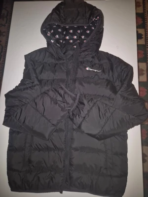 Svart dunjacka från Champion XL - Svart dunjacka från Champion. Jackan är nästan helt ny och är bara använd ett fåtal gånger. Storleken är XL i barnstolek/tonåring.