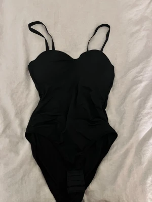 Svart body med smala axelband - Stilren svart body med smala, justerbara axelband och lätt vadderade kupor. Klassisk och enkel design som passar perfekt till stranden eller poolen. Materialet känns mjukt och följsamt mot kroppen. Det är en M/38 men sitter som en s/36 & därav säljer jag den. Aldrig användt utan enbart testat på. Kostar 140kr vanligtvis. 