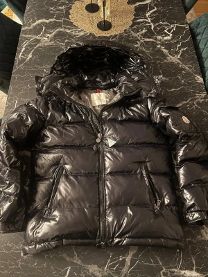Svart pufferjacka från Moncler - Hej! Jag säljer min Moncler Maya som är i nyskick. Den är helt ny och oanvänd, och har ej några skador eller repor! Ny pris ca 16000kr. Jag säljer min för 2499! Jag fraktar jackan sammadag om det är före 18, annars ör det dagen efter!!!📦