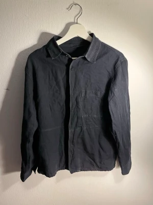 Mörkblå overshirt med bröstficka - Stilren overshirt med en najs mörkblå stvättad färg i bomull med klassisk krage och en enkel bröstficka. Rak passform och diskreta sömmar ger ett minimalistiskt intryck. 
