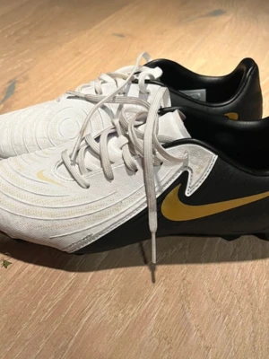 Nike Phantom GX II Academy, st. 38,5 - Snygga fotbollsskor från Nike i vitt och svart med guldiga detaljer, använda en gång. Storlek 38,5