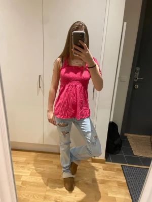 Rosa smockad linnetopp - Snygg rosa linnetopp med smockad överdel och lös passform nedtill. Toppen är ärmlös och har tunna axelband, perfekt för varma dagar. Materialet känns lätt och luftigt, vilket gör den superbekväm att bära.