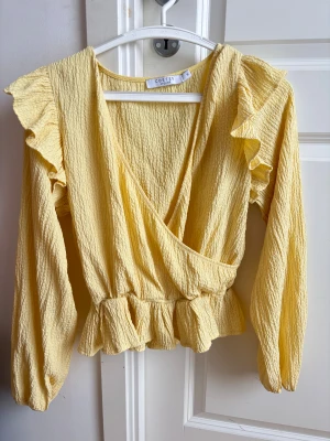 Gul omlottblus från Costes Atelier - Omlottblus från Costes Atelier med volangdetaljer vid axlar och midja. Endast använd vid ett tillfälle💛