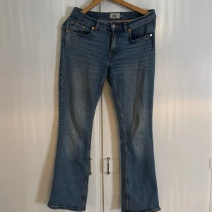 Blå bootcut jeans från 157, storlek S - Bootcut jeans i klassisk blå tvätt från 157, modell Lowboot. Jeansen har fem fickor, orangea sömmar och normal passform. Materialet är jeans med lätt slitning framtill och bakfickor. Perfekt för dig som gillar retrovibbar och snygg siluett.