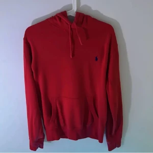 Röd hoodie från Polo Ralph Lauren - Snygg röd hoodie från Polo Ralph Lauren med klassisk blå broderad logga på bröstet. Tröjan har huva med snörning, stor magficka och långa ärmar. Materialet är en mjuk blandning av bomull och polyester, perfekt för en stilren look! Pris går att diskutera!