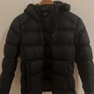 Svart pufferjacka från Everest - Svart pufferjacka från Everest med huva och dragkedja framtill. Jackan har en quiltad design med breda kanaler och långa ärmar. Priset går att diskuteras🩷
