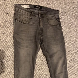 Replay Rocco grå jeans, comfort fit - Snygga grå jeans från Replay, modell Rocco med comfort fit. Klassisk femficksdesign, svarta detaljer och Replay-logga på bakfickan. Jeansen har raka ben och är tillverkade i mjukt jeanstyg för extra komfort. Perfekt för dig som gillar stilrena och bekväma jeans.