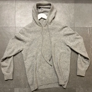 Grå stickad hoodie med huva - Mysig grå kashmir hoodie med ribbade muddar och en stilren design som funkar till det mesta. Tröjan är perfekt för kyligare dagar nu när hösten har kommit. Den här två defekter där av det låga priset!