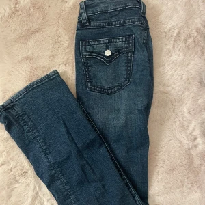 Mörkblå jeans med bakficka - Mörkblå jeans med coola kontrastsömmar och dekorativ bakficka med knapp. Klassisk femficksmodell i mjukt tyg. De är utsvängda. Strl 164 men sitter som XS