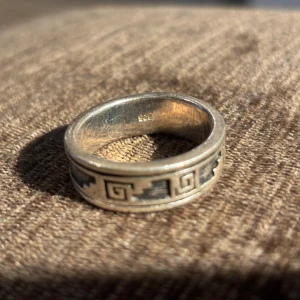 Äkta silverring 925 – grekiskt/aztekiskt mönster - Snygg och tidlös ring i äkta sterlingsilver (925) med ett vackert grekiskt nyckel- eller aztek-inspirerat mönster runt hela ringen.	Tillverkning: Handgjord (vanligt i Mexiko eller Peru) Ringen är robust, bekväm att bära och har en unik vintagekänsla med lätt patina som ger den extra karaktär.