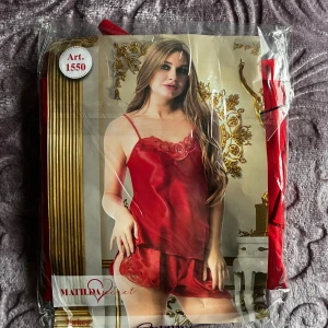 Röd satin linnetopp från Matilda Secret - Säljer en röd linnetopp med shorts i satin från Matilda Secret med tunna axelband och dekorativ spets upptill. Toppen har en glansig finish och är perfekt för dig som gillar en feminin och lyxig look. Matchande shorts med spetsdetaljer ingår.