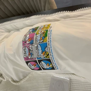 Vit Moncler cardigan finns alla storlekar  - Säljer en snygg vit dunjacka från Moncler med ribbade ärmar och huva. Jackan har dragkedja framtill, quiltad kropp och coolt Moncler-märke på ärmen. Insidan har ett färgglatt serietryck. Perfekt för dig som vill ha en clean och exklusiv look.