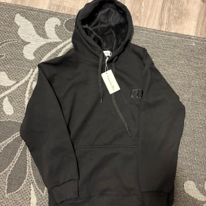 Svart hoodie från Christian Dior - Svart hoodie från Christian Dior med broderad CD-logga på bröstet. Tröjan har huva med snörning, mjuk insida och klassisk känguruficka framtill. Perfekt för dig som gillar stilrena och exklusiva streetwear-plagg.