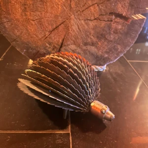 Okänd elektronikprodukt - Unik och robust konstruktion av metall, troligen en konstnärlig eller mekanisk prydnad. Objektet har flera cirkulära, tandade skivor och en metallisk nos, vilket ger ett igelkottsliknande utseende. Inga synliga elektroniska komponenter eller märkning.