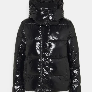 Svart pufferjacka Calvin Klein  - Säljer en svart, glansig pufferjacka från Calvin Klein med huva och diskret CK-logga på bröstet. Jackan har dragkedja, stora fickor och quiltad design. Perfekt för kalla dagar och har en najs model.