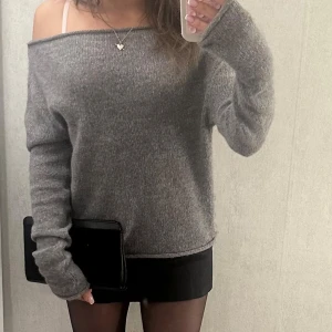 Grå offshoulder stickad tröja - Mysig grå stickad tröja med offshoulder-modell och långa ärmar. Tröjan har en loose passform och är perfekt för dig som gillar en avslappnad men ändå trendig look. Passar snyggt till kjol eller jeans och är superenkel att styla.