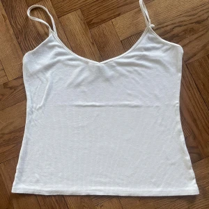 Vit ribbad linnetopp från Carin Wester - Säljer en vit ribbad linnetopp från Carin Wester i storlek M. Toppen har smala axelband och en snygg v-ringad halsringning. Materialet är mjukt och stretchigt med 96% viskos och 4% elastan, vilket gör den riktigt skön att bära. Perfekt för varma dagar och enkel att styla.