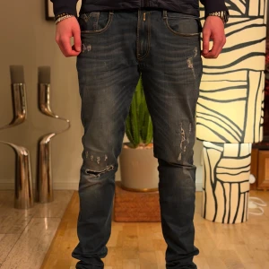 Replay Anbass blå slitna jeans - Säljer ett par Replay Anbass jeans i blå tvätt med slitningar och snygga detaljer. Jeansen har klassisk femficksdesign, kontrastsömmar och broderade bakfickor. Modellen är rak med normal passform och tillverkad i mjukt jeanstyg.