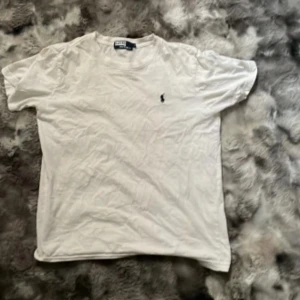 Vit t-shirt från polo Ralph lauren - Vit t-shirt från Polo Ralph Lauren i 100% bomull. Klassisk design med korta ärmar och rund hals. På bröstet finns den ikoniska broderade Polo-loggan i mörkblått. Perfekt för en clean och stilren look. Det är storlek L på barn!