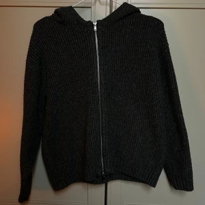 Mörkgrå stickad hoodie från BikBok - Mysig mörkgrå stickad hoodie från BikBok i ribbat material. Tröjan har dragkedja framtill, huva och långa ärmar 🌟
