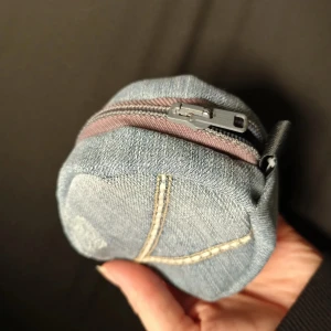 Rund plånbok i ljusblå denim - Snygg rund plånbok i ljusblå denim med dekorativa sömmar och en praktisk dragkedja. Perfekt att ha småsaker i och lätt att fästa med metallklämman. Jeansmaterialet ger en cool och avslappnad vibe.