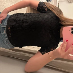 Svart spetsblus med kort ärm - Säljer en svart blus i spets med korta ärmar och rund hals. Blusen har ett genombrutet blommigt spetsmönster som ger en snygg och feminin vibe. Perfekt att styla med jeans eller kjol för en cool look. Fråga gärna om fler bilder eller mått!
