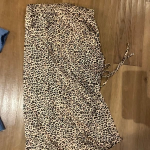 Leopardmönstrad omlottkjol med snörning - Säljer en lång omlottkjol med leopardmönster i beige och svart. Kjolen har snörning i midjan för en justerbar passform och är tillverkad i ett lätt och mjukt material som ger en skön känsla. Perfekt för dig som vill sticka ut med ett djuriskt print.