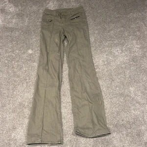 Gröna bootcut-byxor från H&M Divided - Snygga gröna bootcut-byxor från H&M Divided i storlek 32. Byxorna har fickor med lock och knapp framtill samt en extra ficka med dragkedja. Tillverkade i bomull med lite stretch för skön passform. Perfekt för dig som gillar retrovibbar och coola detaljer.