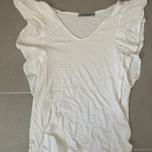 Vit v-ringad t-shirt från Å - Vit t-shirt från Å i storlek XS med v-ringad hals och korta ärmar. Tillverkad i mjuk bomull, perfekt för en chill och enkel stil. Passformen är normal och tyget är tunt och skönt mot huden. Den är lite genomskinlig😊kan passa större storlekar