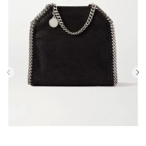 Svart axelväska från Stella McCartney - Helt nytt skick och säljer för nästan halva priset. Cool svart axelväska från Stella McCartney med kedjedetaljer i silver runt kanterna och som axelrem. Väskan har en mjuk, glansig yta i syntetmaterial och ett ljusrosa foder med logotyp. Perfekt för dig som vill ha en edgy och trendig look. Passar perfekt till skolan för mappar och dator. 