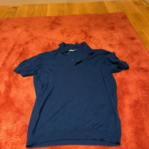 Marinblå pikétröja från A Days March - Snygg marinblå pikétröja med klassisk krage och två knappar framtill. Tröjan har korta ärmar och är tillverkad i ett mjukt material som känns skönt mot huden. Perfekt för dig som gillar enkel och stilren design.