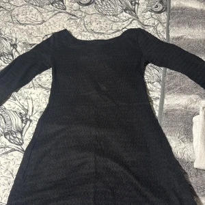 Svart långärmad klänning med snörning - Svart långärmad klänning med snygg snörning framtill och dekorativa pärlor i ändarna. Materialet är tunt och lätt transparent med en diskret struktur. Klänningen har en rundad halsringning och sitter figurnära över kroppen.