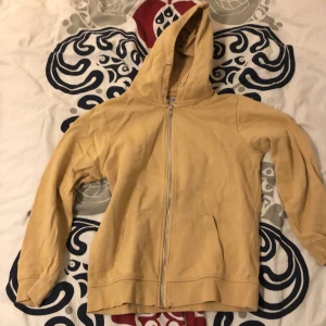 Beige hoodie med dragkedja från 157 - Säljer en beige hoodie från 157 med dragkedja framtill och stor huva. Tröjan har två fickor på magen och är tillverkad i mjuk bomull. Perfekt för chill dagar och enkel att matcha med jeans eller mjukisbyxor.